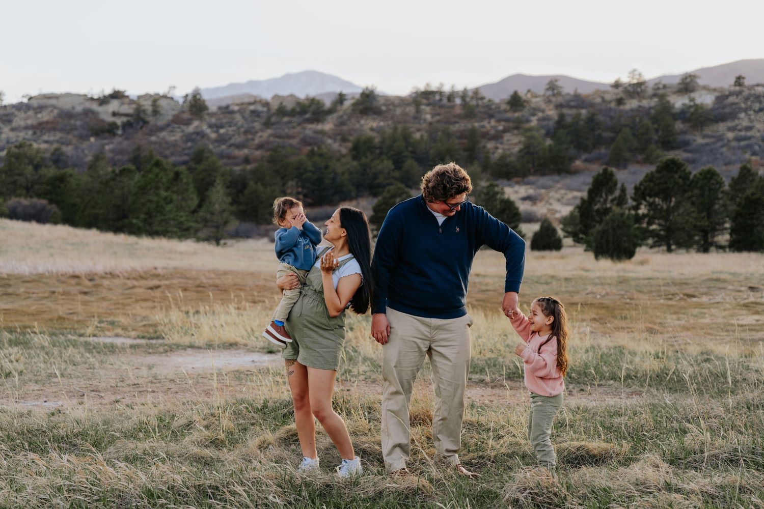 Family of four walking and laughing together in a scenic mountain meadow.