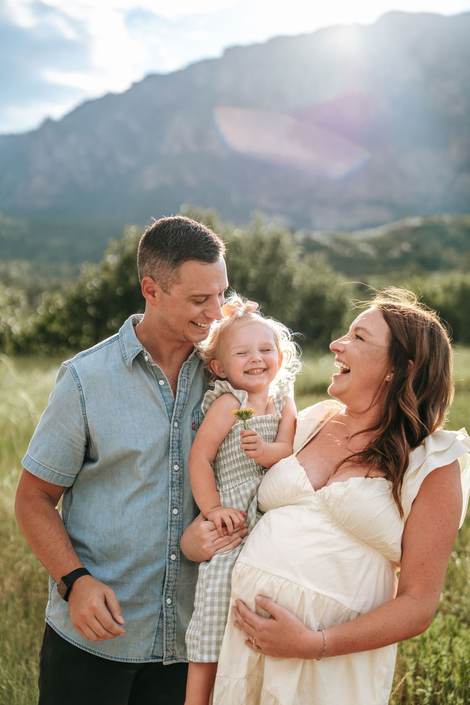 A happy family with a toddler laughs together in a sunlit meadow with red rock mountains.