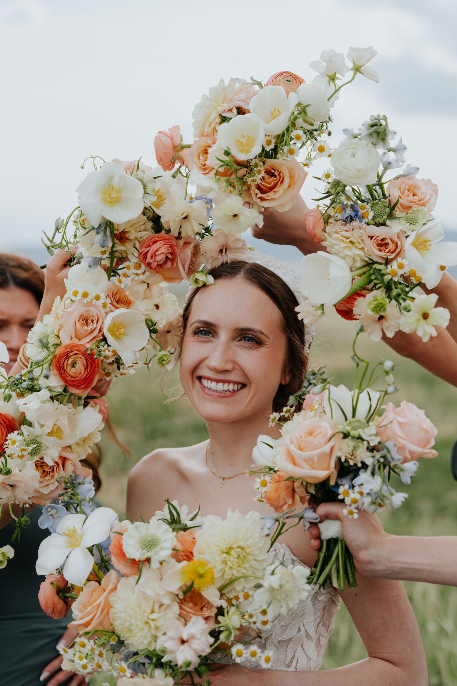 Smiling bride surrounded by colorful peach and white floral bouquets held in a circle around her face.
