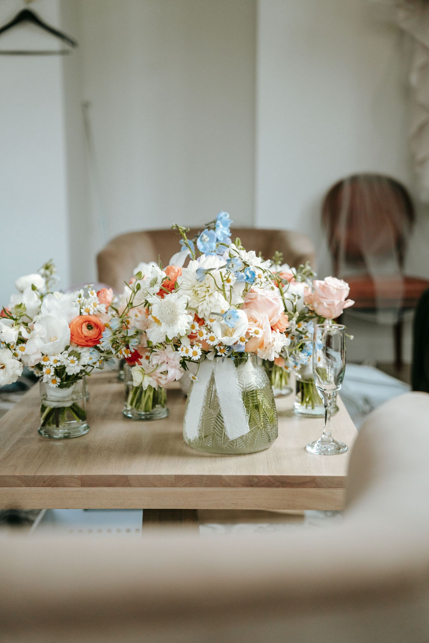 Elegant wedding bouquets with pink, white, and blue flowers arranged in glass vases on wooden table.
