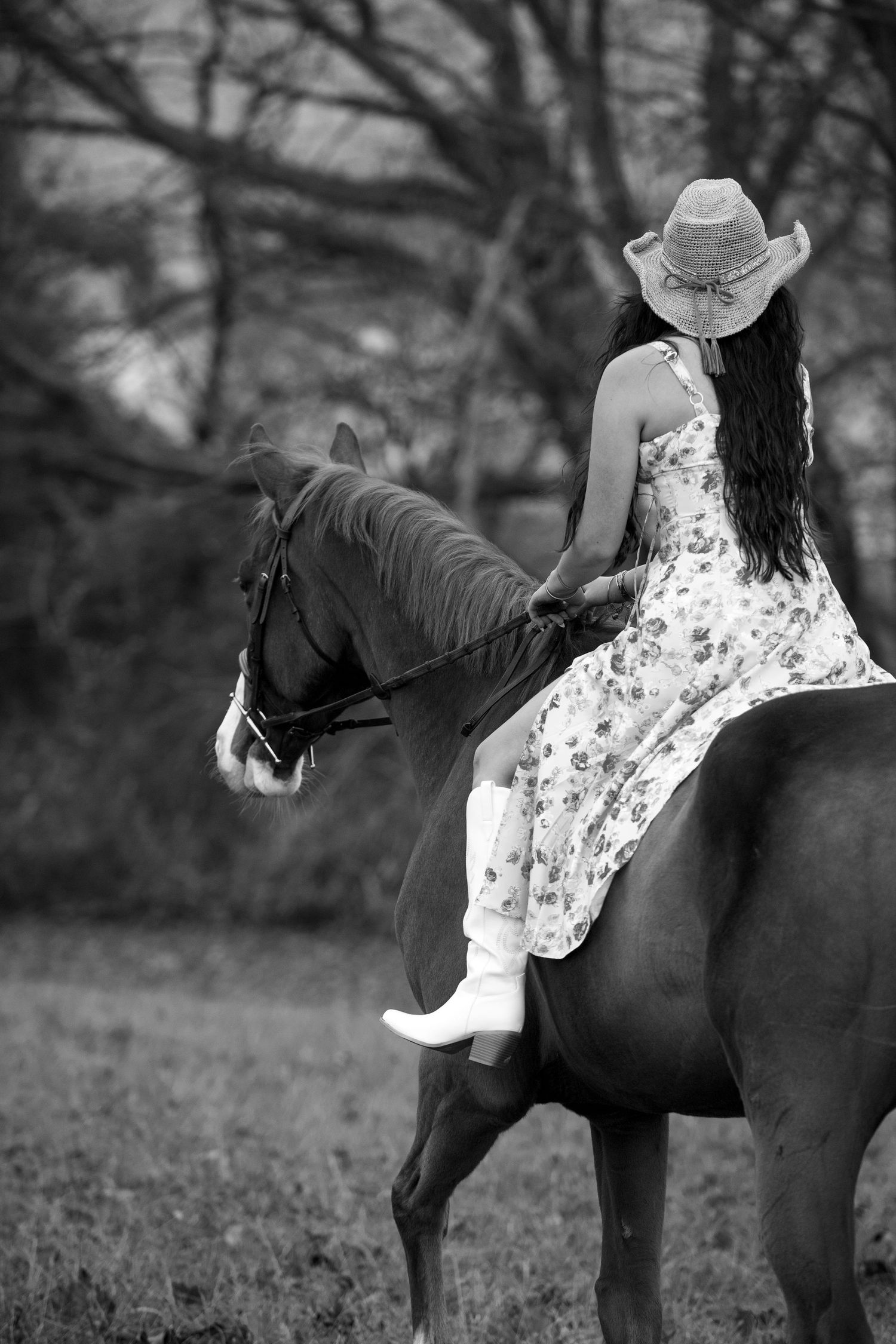 Rider in floral dress and cowboy hat sits sidesaddle on a dark horse in black and white photography.