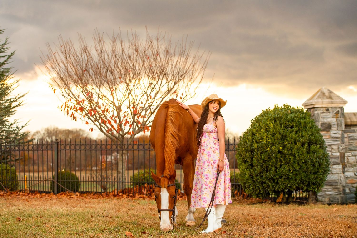 Horse and companion in floral dress posing near stone wall and garden.