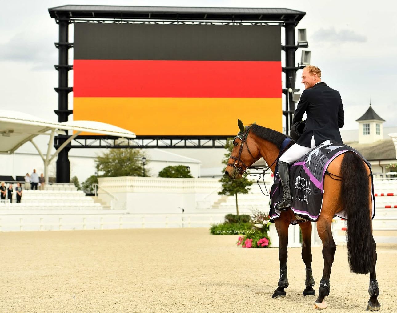 Horse and rider posed in front of large electronic scoreboard displaying German flag colors.