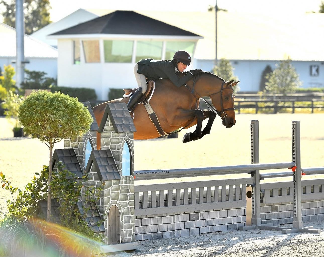 Show jumper soaring over stone wall obstacle during daytime competition.