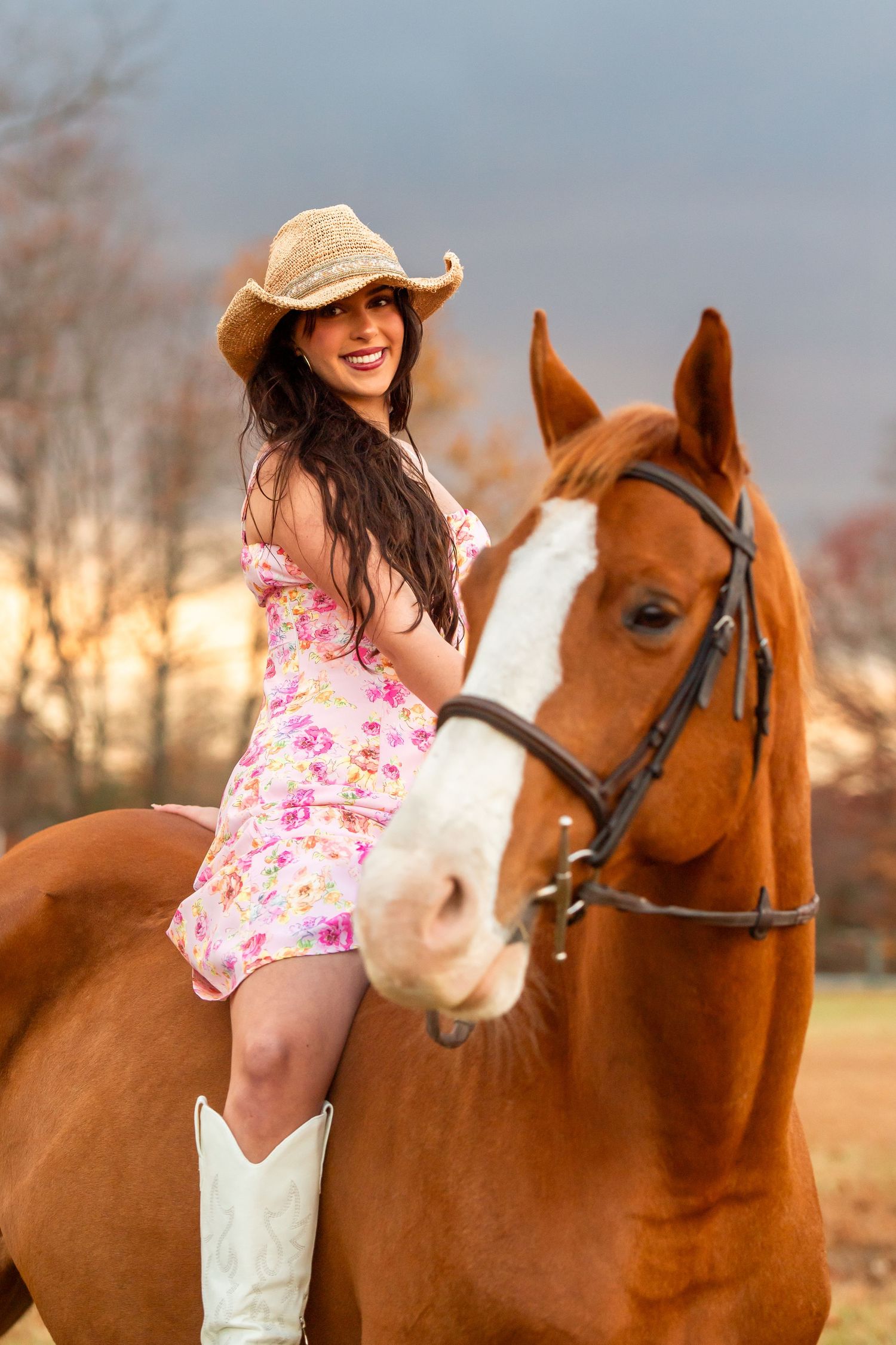 Chestnut horse with white blaze poses with companion in floral dress and cowboy boots.