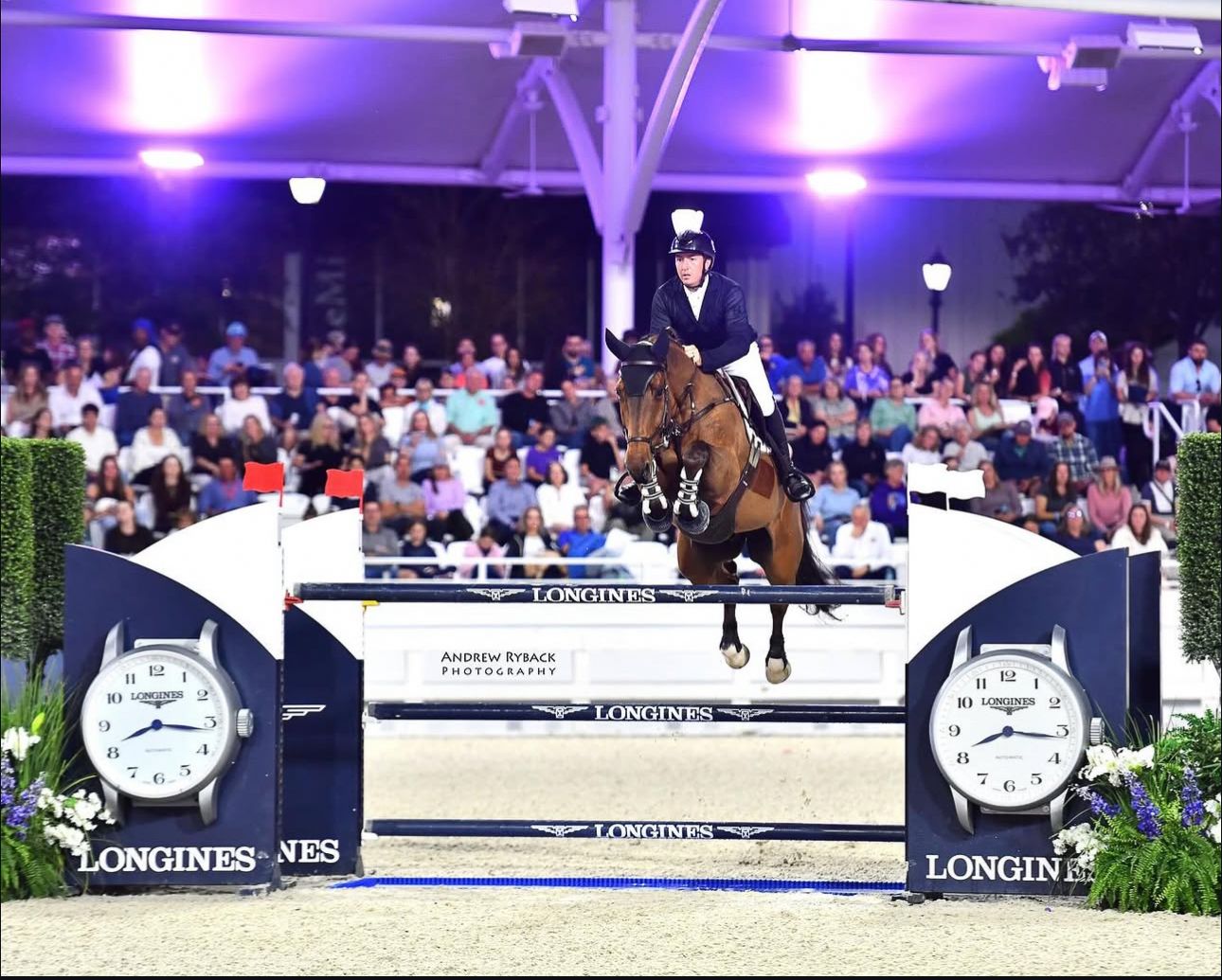 Horse and rider competing in illuminated indoor arena with Longines branding and timing displays.