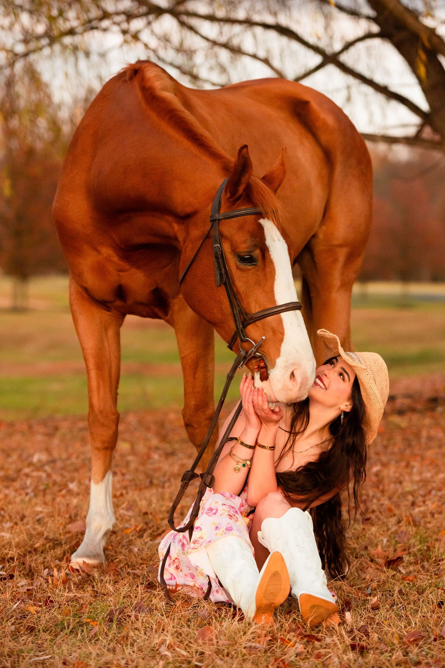 A person in a floral dress and cowboy boots shares an affectionate moment with a chestnut horse.