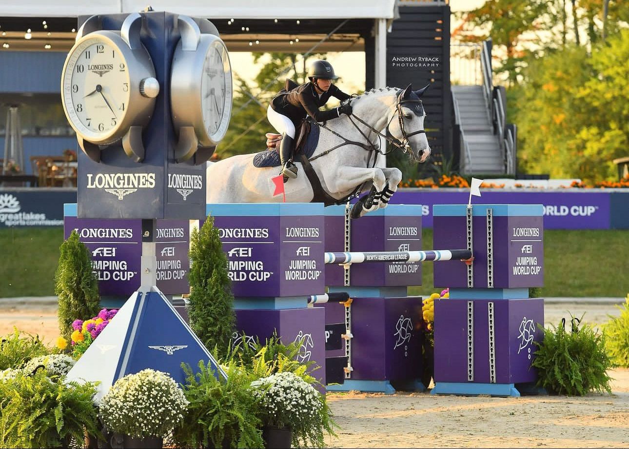 Show jumper clearing purple Longines obstacle during twilight equestrian competition.