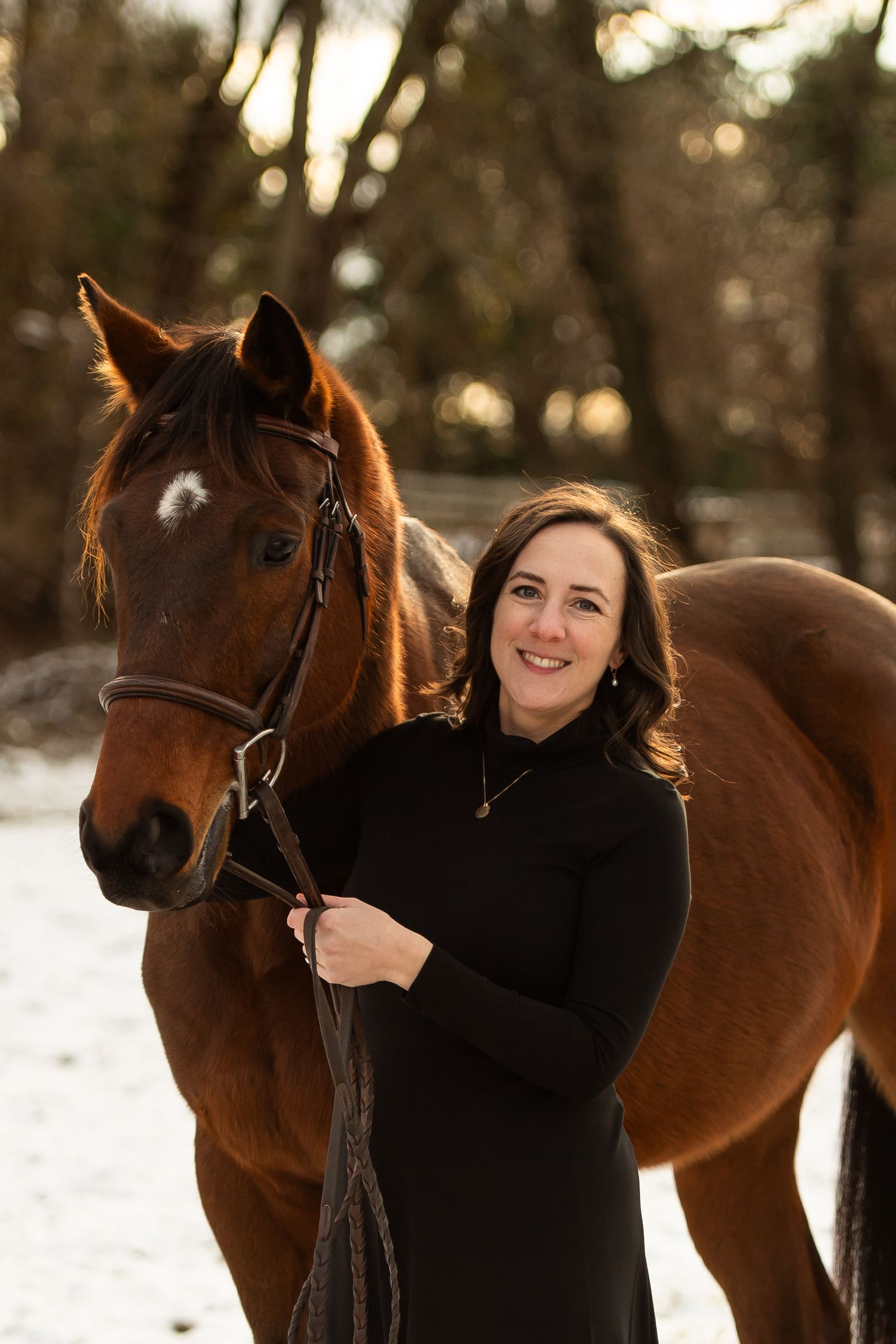 Beautiful bay horse and friend in black sweater pose together in snowy winter forest.