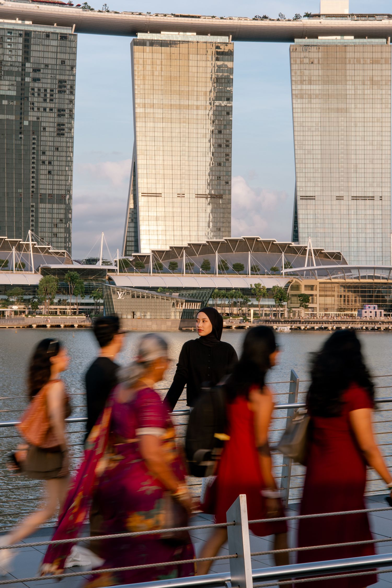 Woman in hijab stands still as blurred pedestrians walk past Marina Bay Sands in Singapore.
