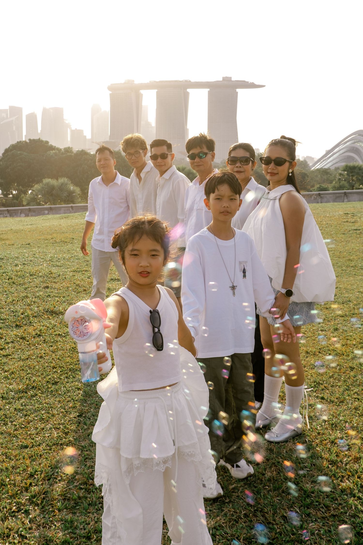 Group of children and adults in white outfits posing with bubbles, Marina Bay Sands Singapore in background.
