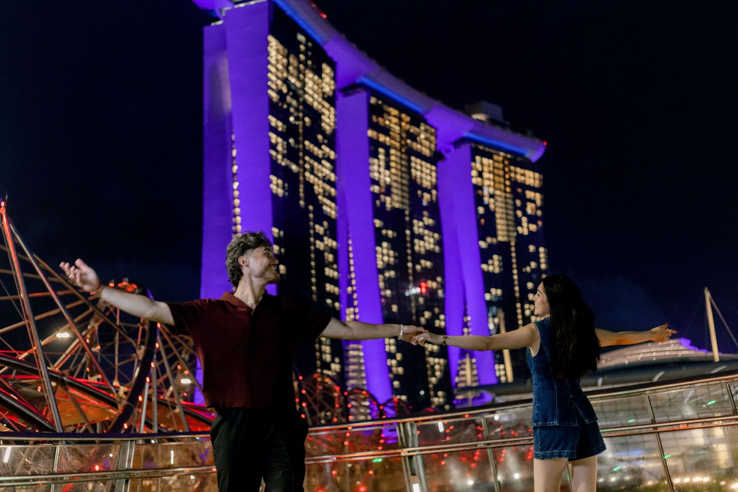 Couple posing at night in front of the illuminated Marina Bay Sands hotel in Singapore.