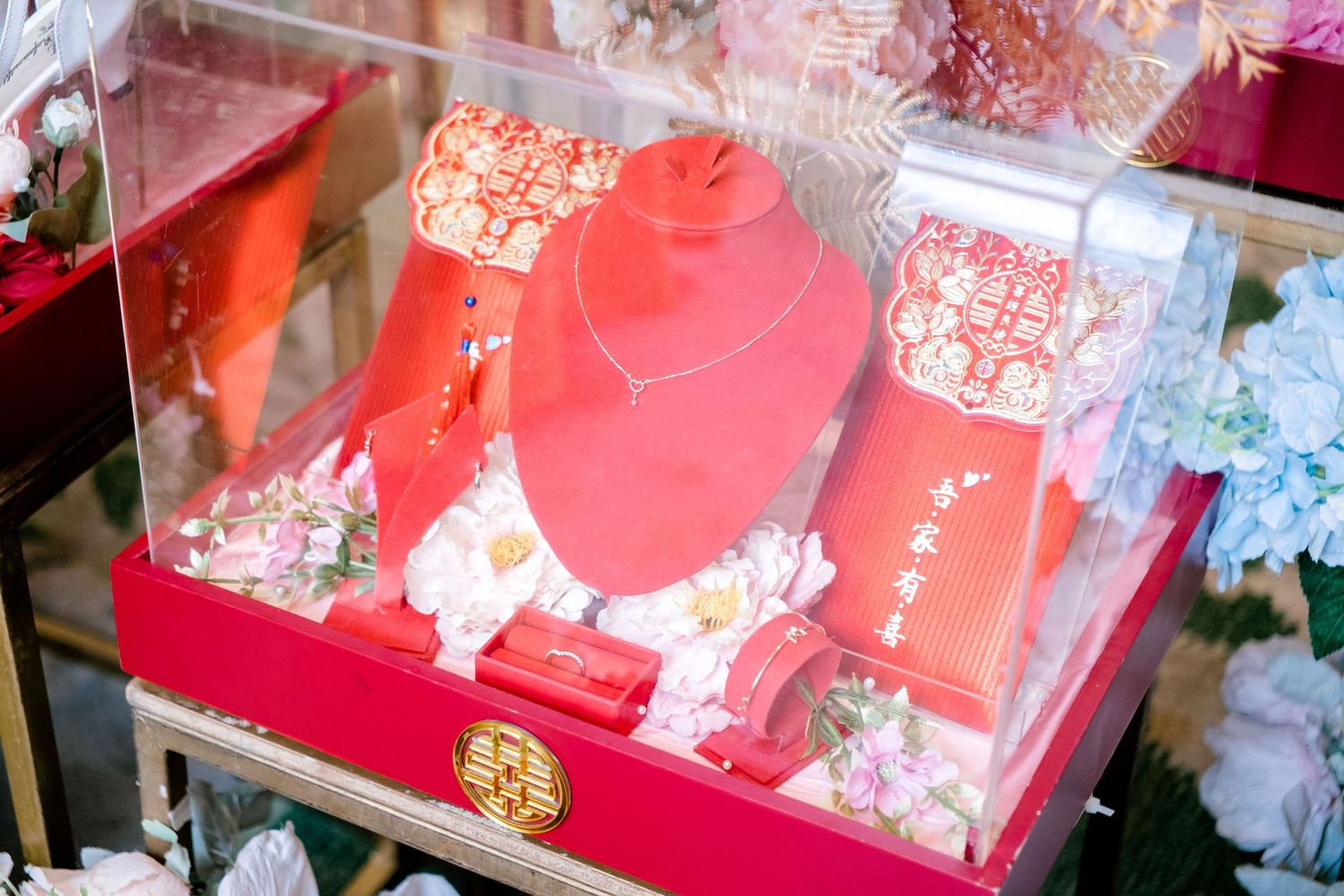 Red velvet display case with Chinese bridal jewelry set including necklace, bracelet, and traditional red accessories.