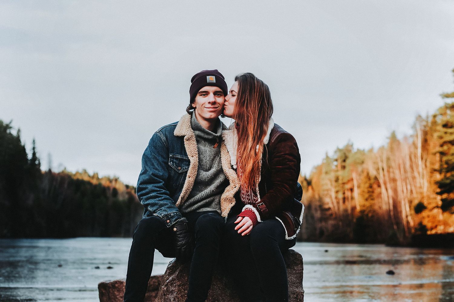 Couple sharing an intimate moment by a lake during autumn sunset.