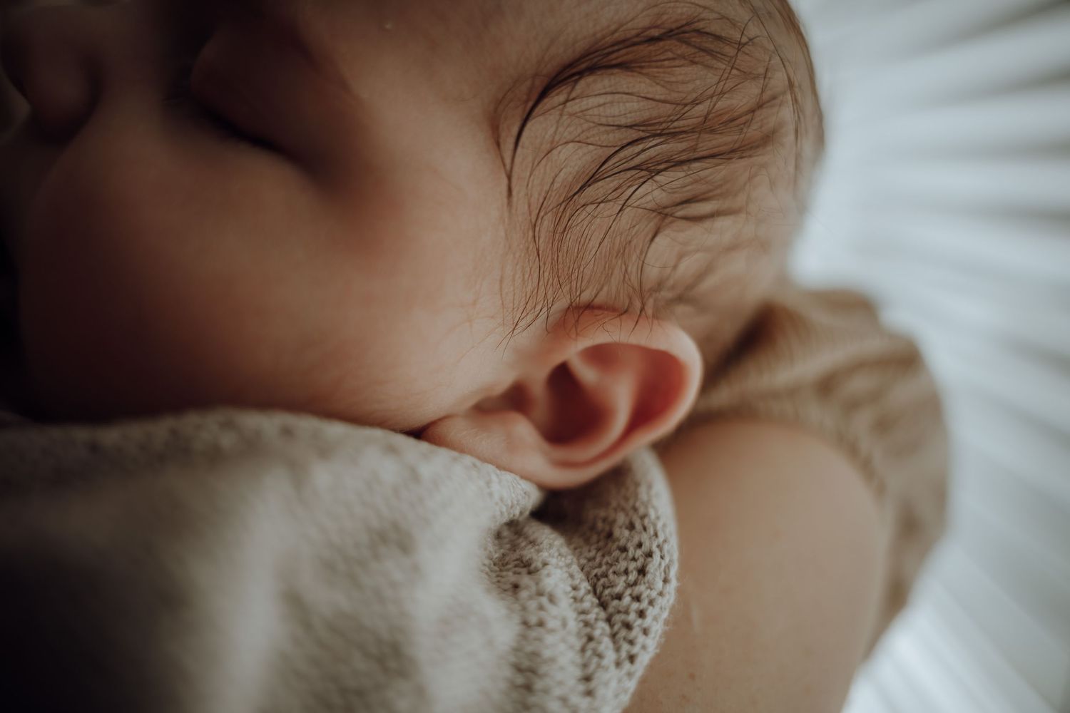 Baby op de arm van moeder, oortjes en haartjes zichtbaar.
