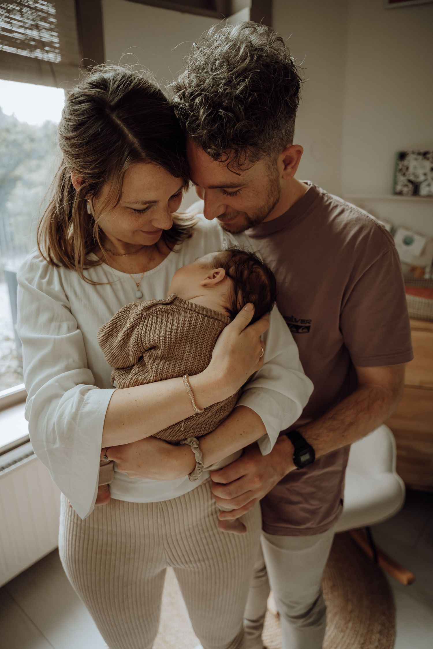 Man en vrouw met hun baby in de armen. Staan knus bij elkaar. In huis.