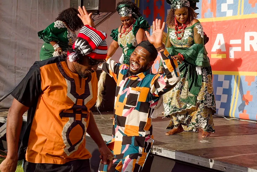 Performers in colorful African traditional costumes dancing energetically on outdoor festival stage.