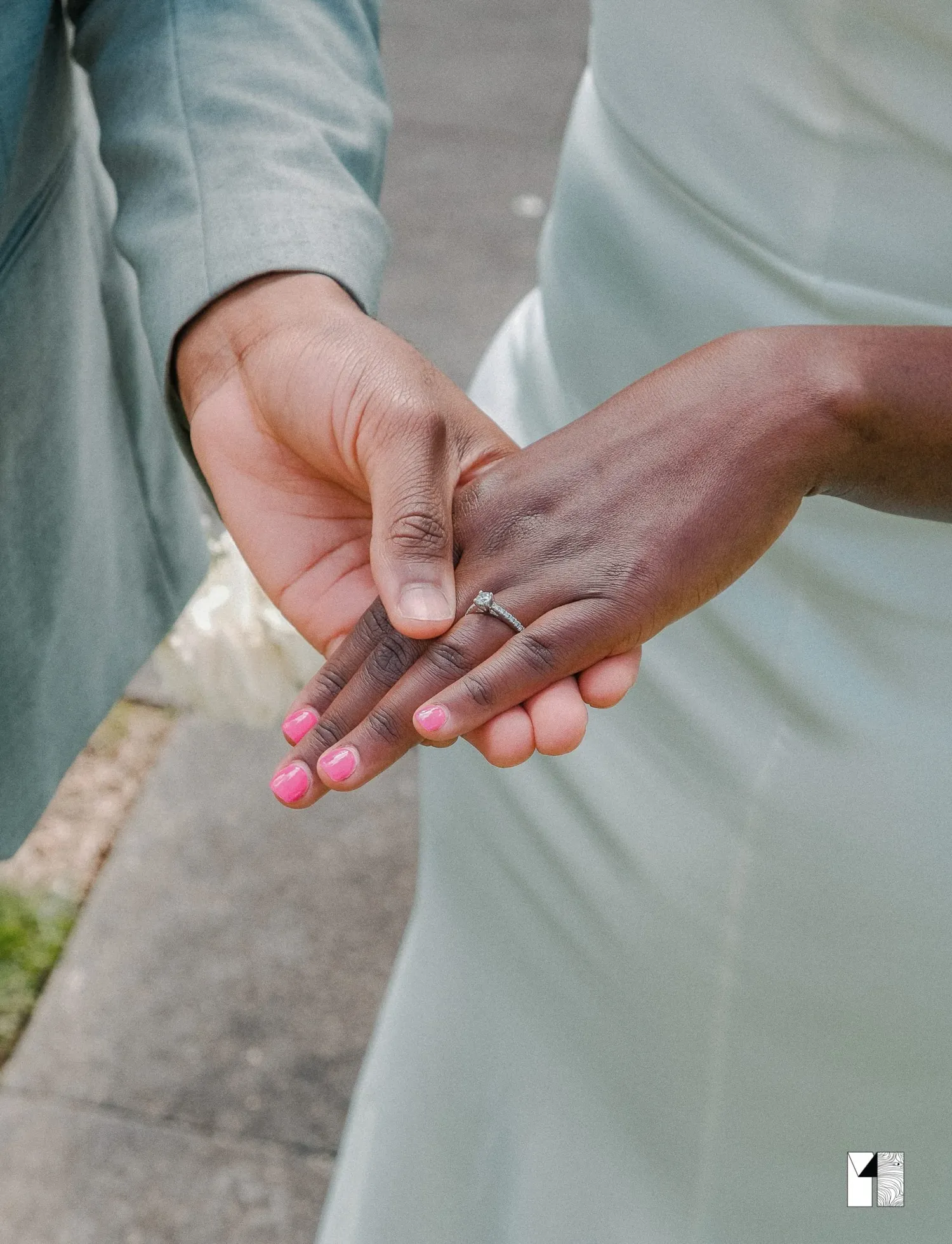 Newlyweds holding hands showing wedding rings, bride with pink nails in a light blue dress.