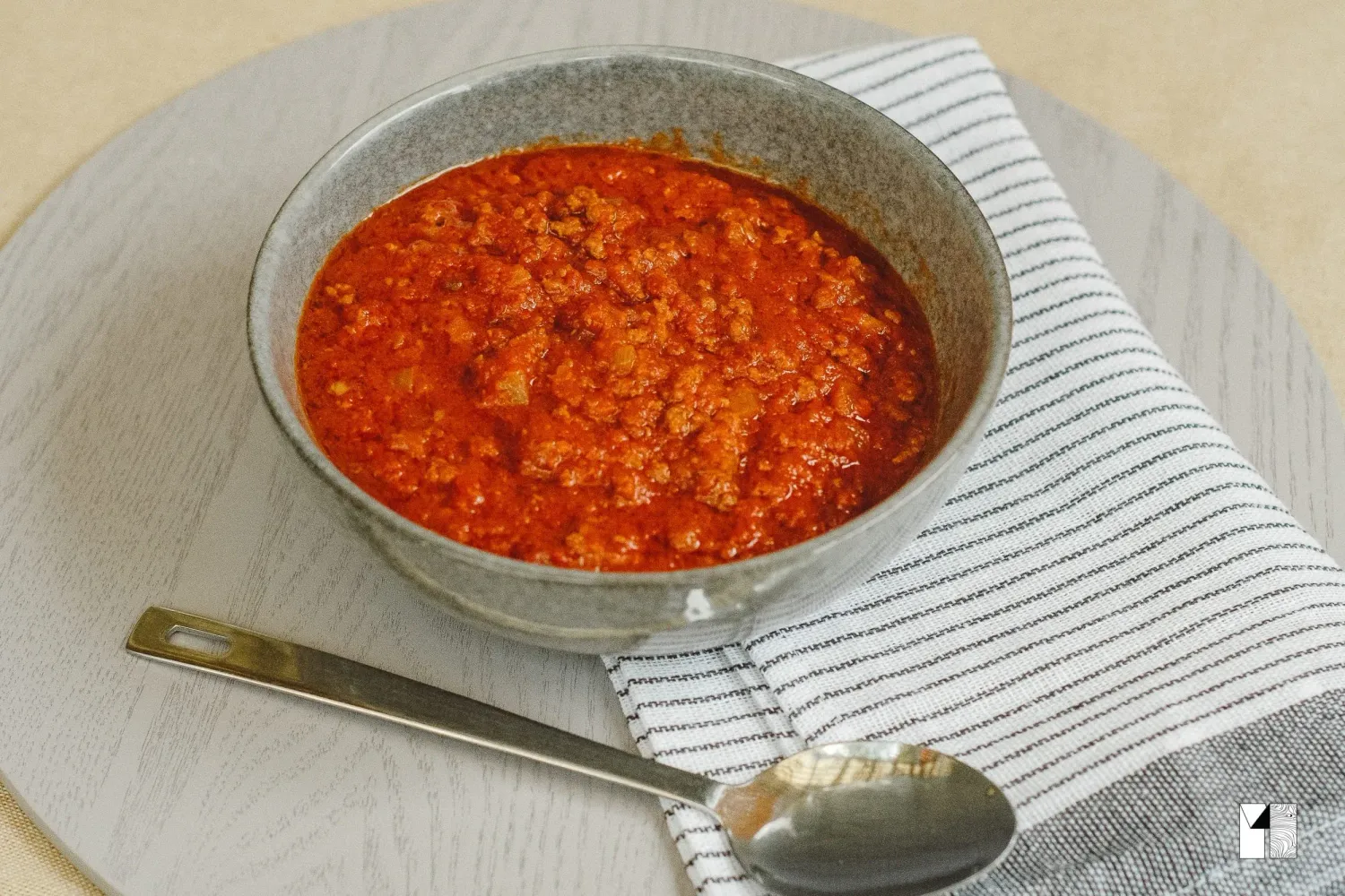 A bowl of hearty tomato meat sauce served with a spoon on a striped cloth napkin.