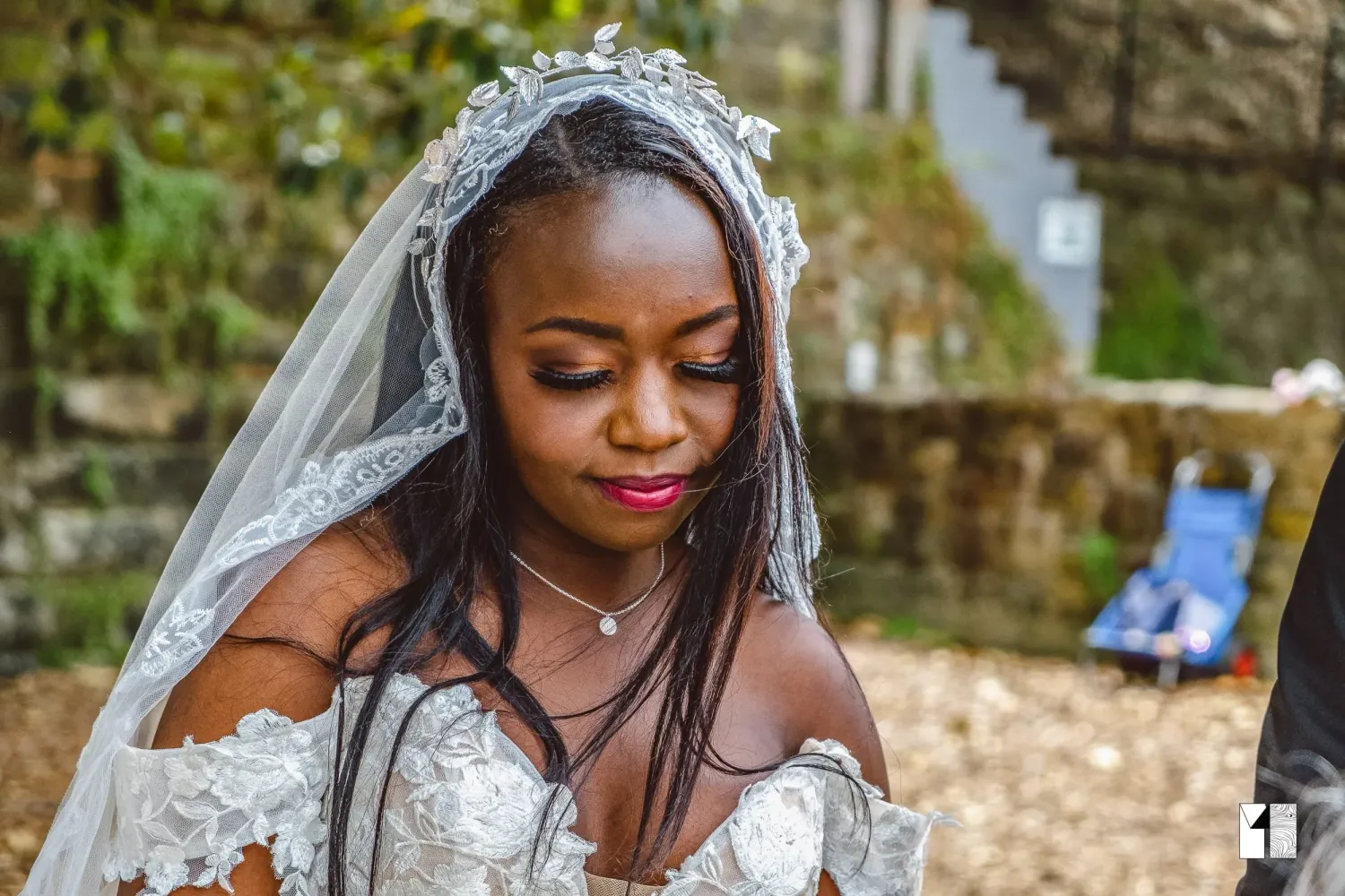Beautiful bride wearing lace veil and off-shoulder wedding dress looks down gracefully.