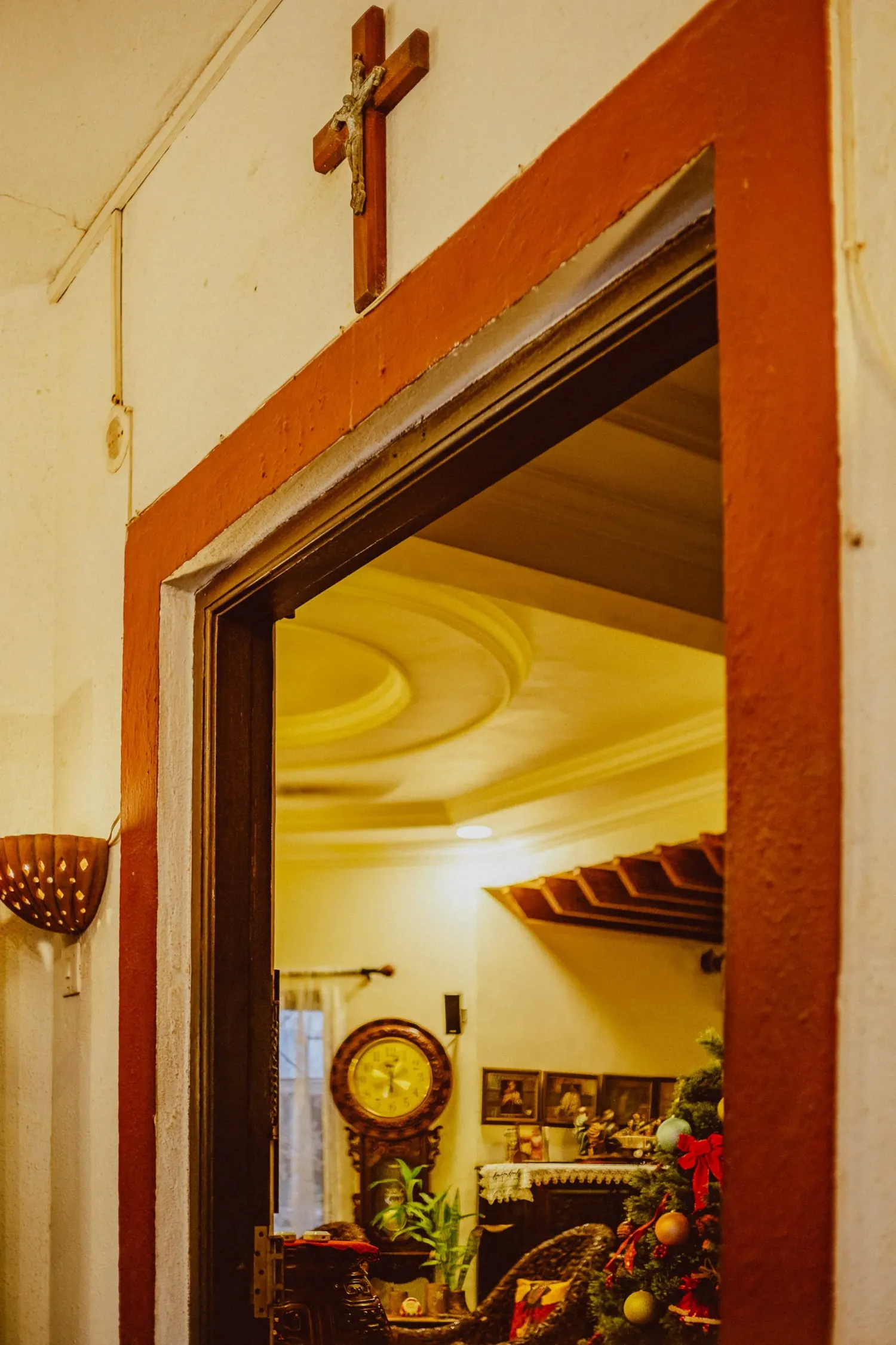 Doorway with wooden crucifix above leading into a warmly lit room with antique clock and decor.