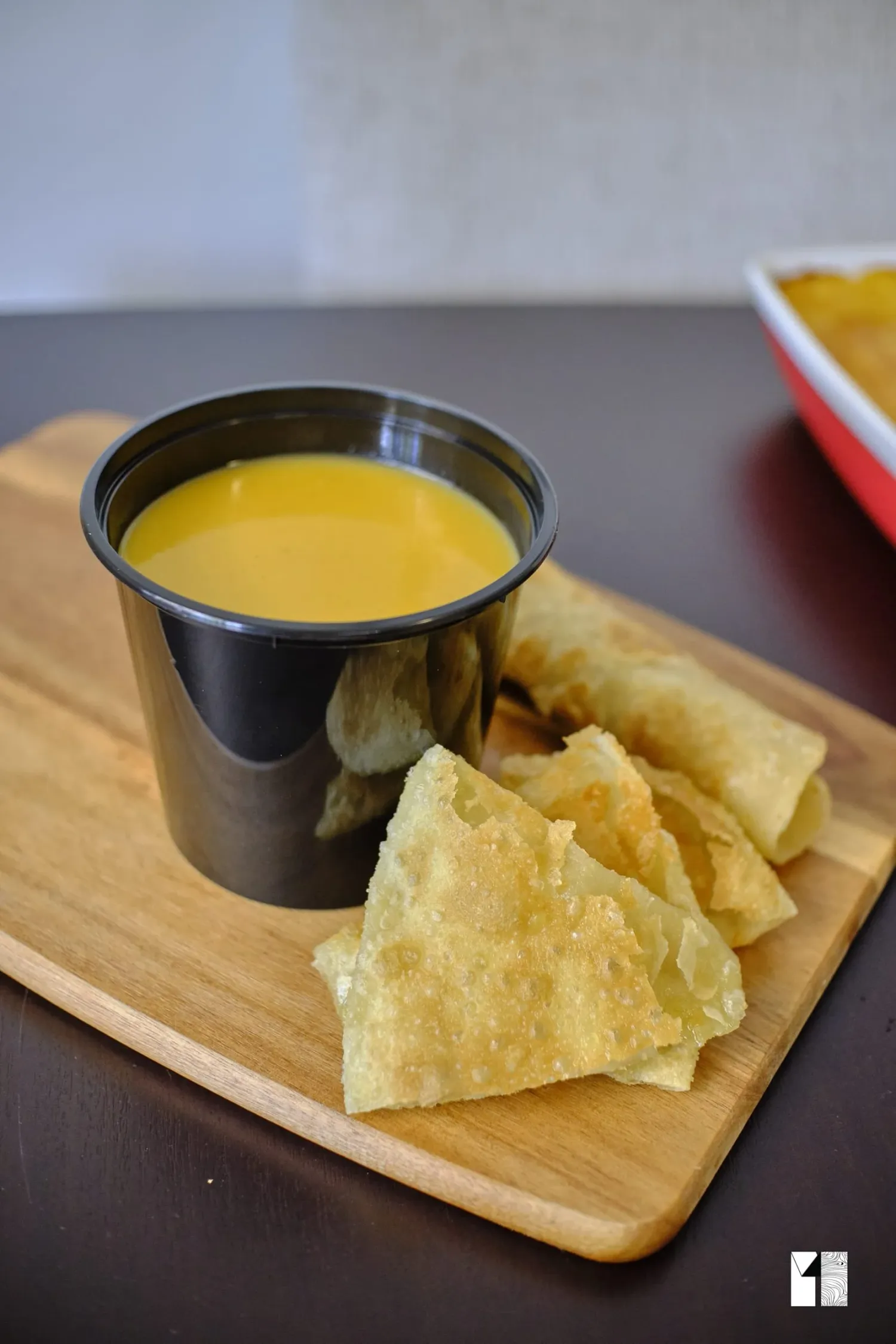 Golden mango dipping sauce in a black cup served with crispy fried wonton chips on a wooden board.
