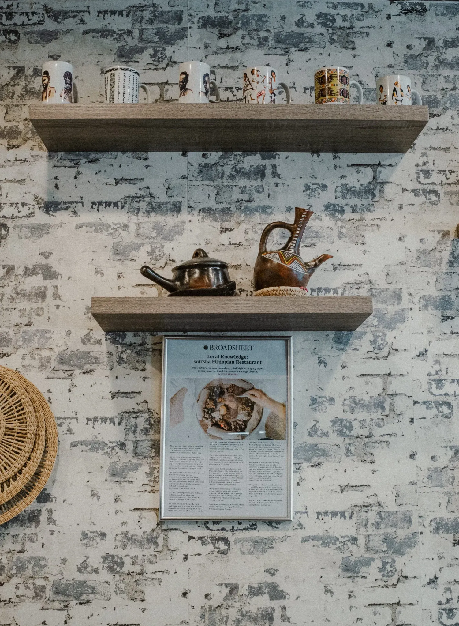 Rustic brick wall shelf displaying traditional Ethiopian clay teapots, mugs, and a framed informational poster.