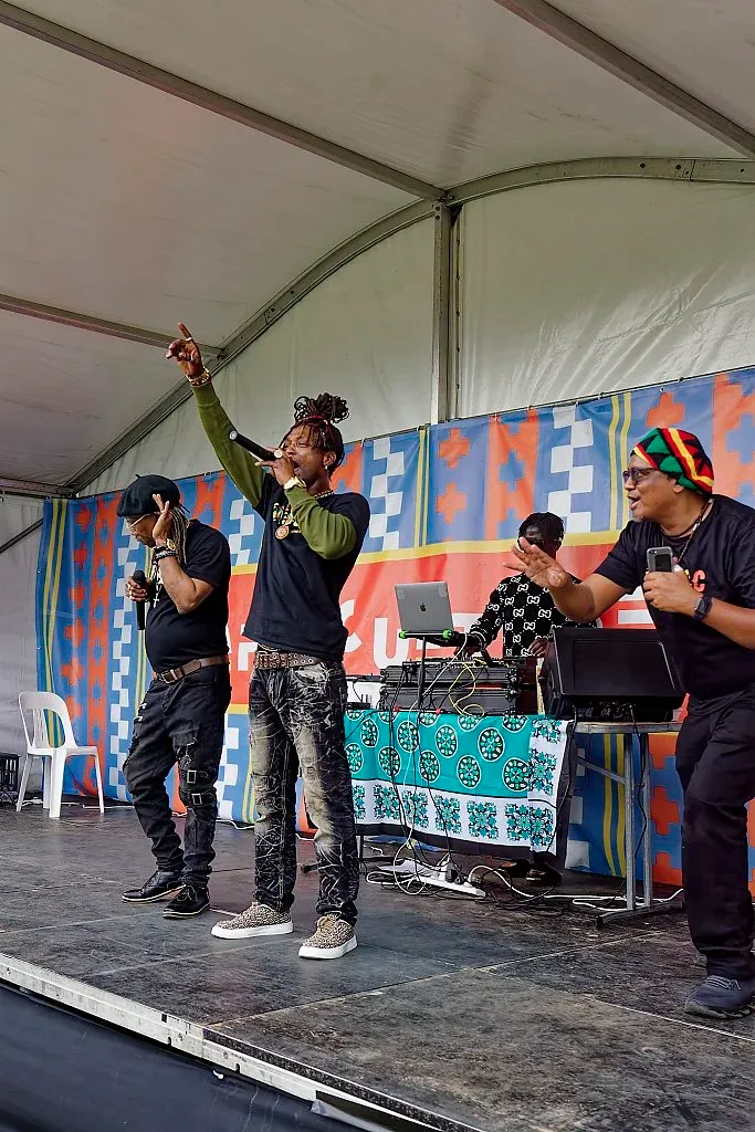 Three performers dancing and rapping on a colorful outdoor festival stage.