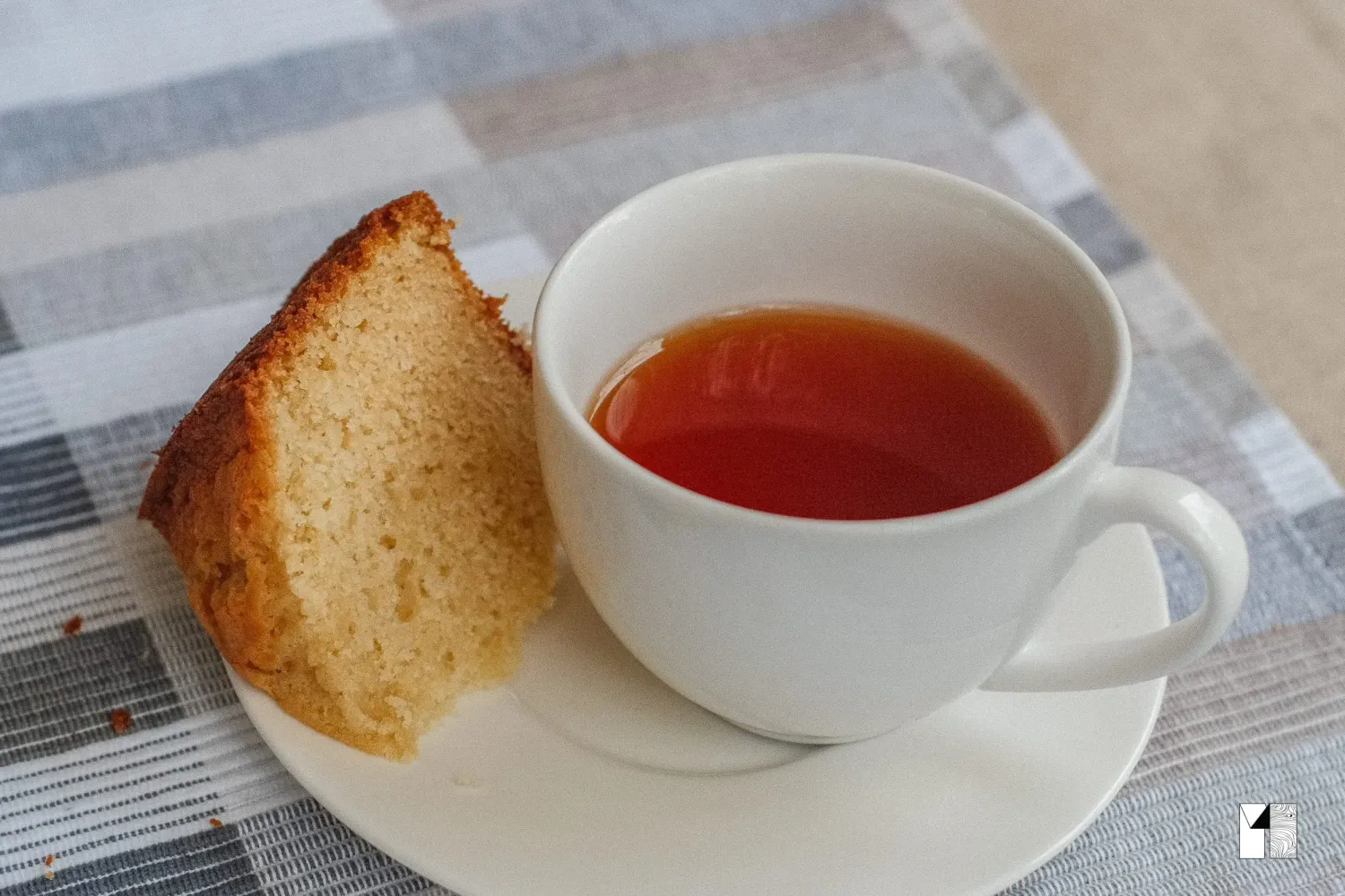 Slice of golden pound cake served alongside a hot cup of tea on a saucer.