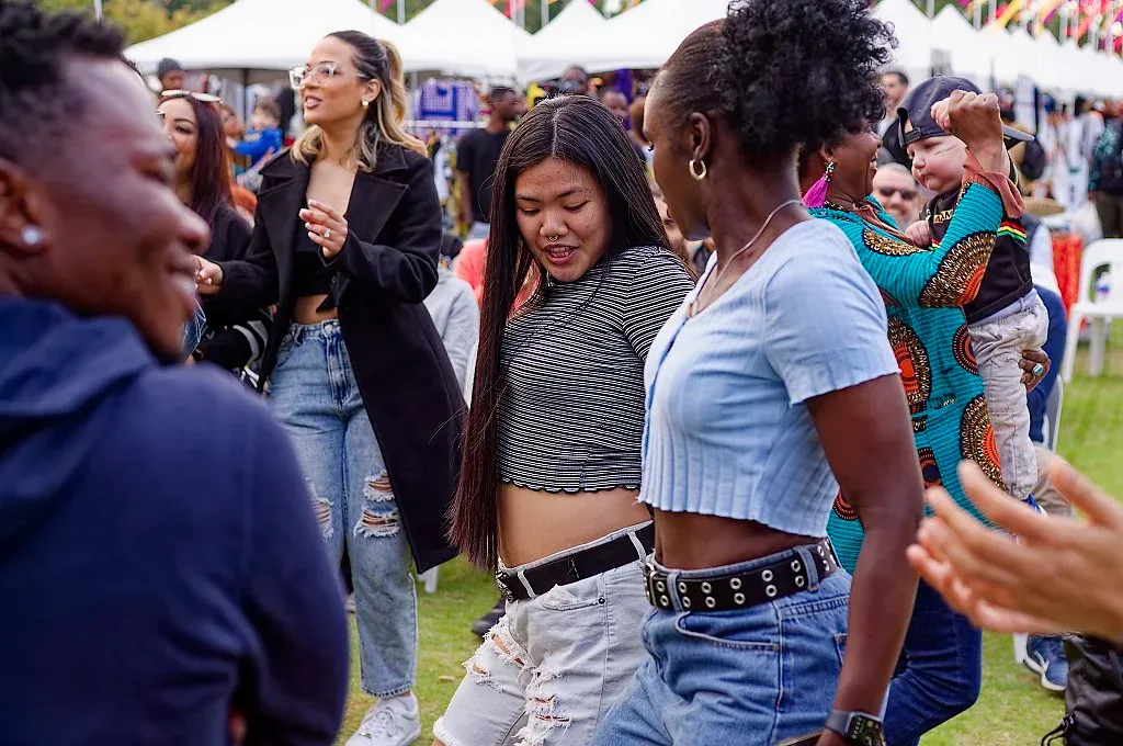 Young women dancing joyfully outdoors at a multicultural festival event.