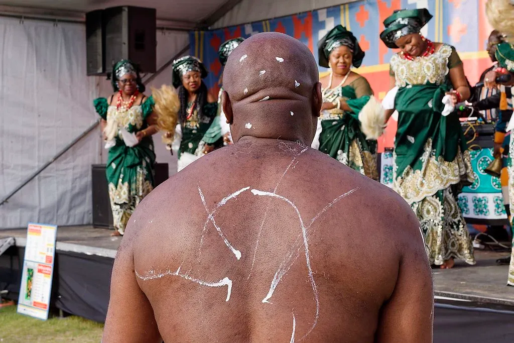 Shirtless man with white body paint watching traditional African dance performance.