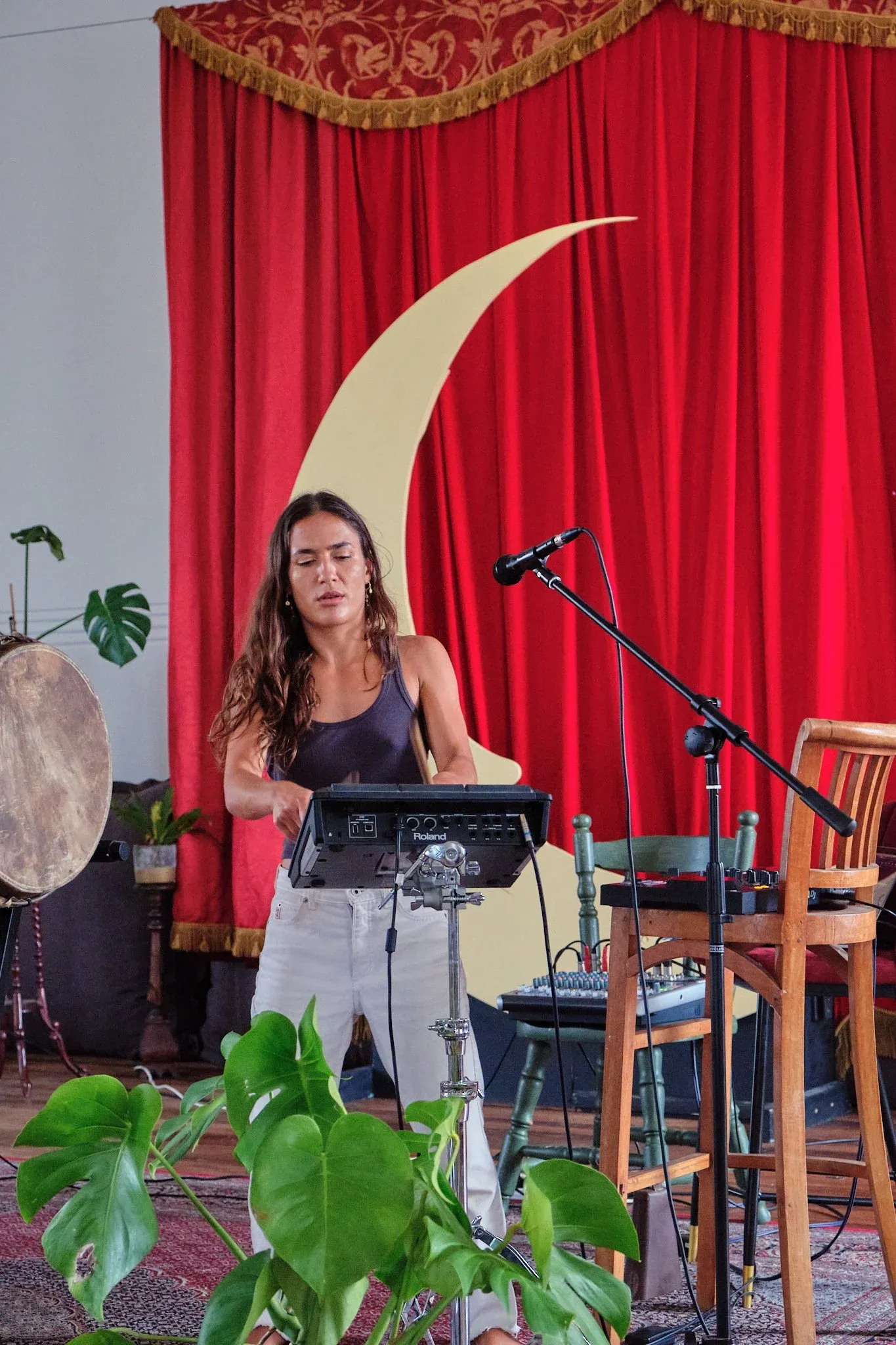 Female musician performing at electronic keyboard setup before red curtain with golden crescent moon decor.