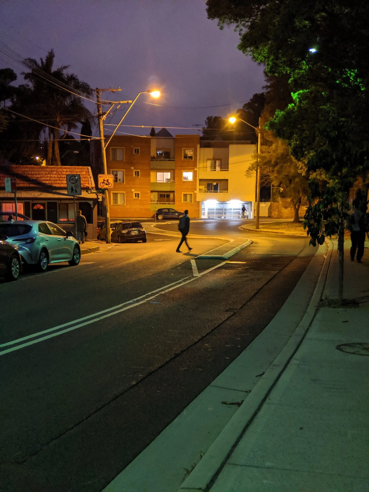 Person crosses an empty street intersection at night under glowing orange streetlights.