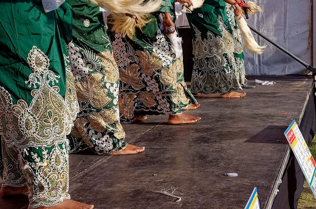 Performers in ornate green and gold embroidered traditional costumes standing on festival stage.