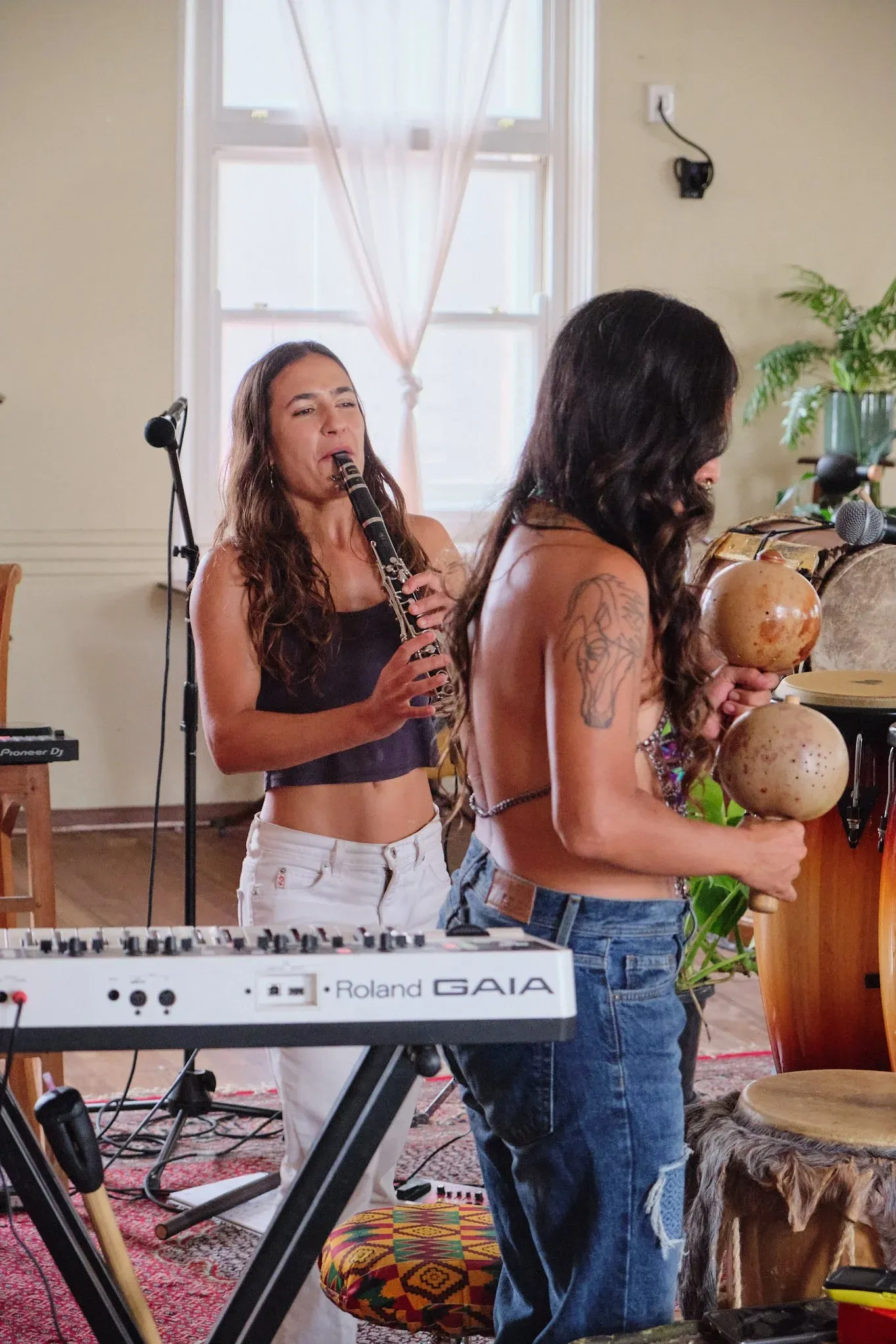 Two young women performing indoors, one playing clarinet near Roland GAIA keyboard, other holding maracas.
