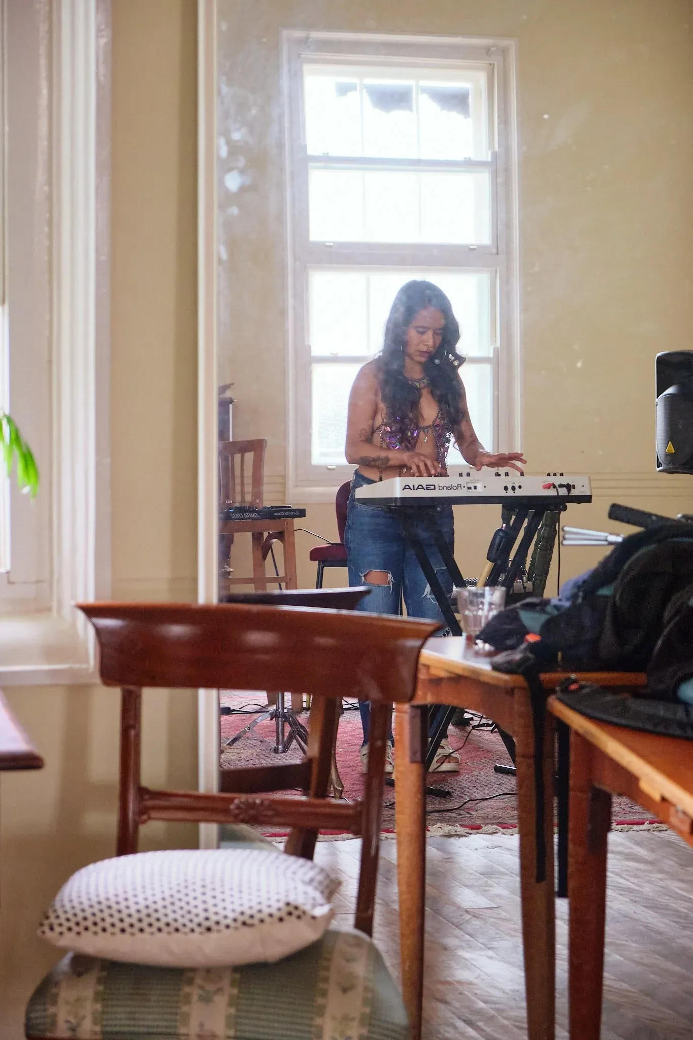 Woman plays a white keyboard synthesizer near a bright window in a warmly lit room.