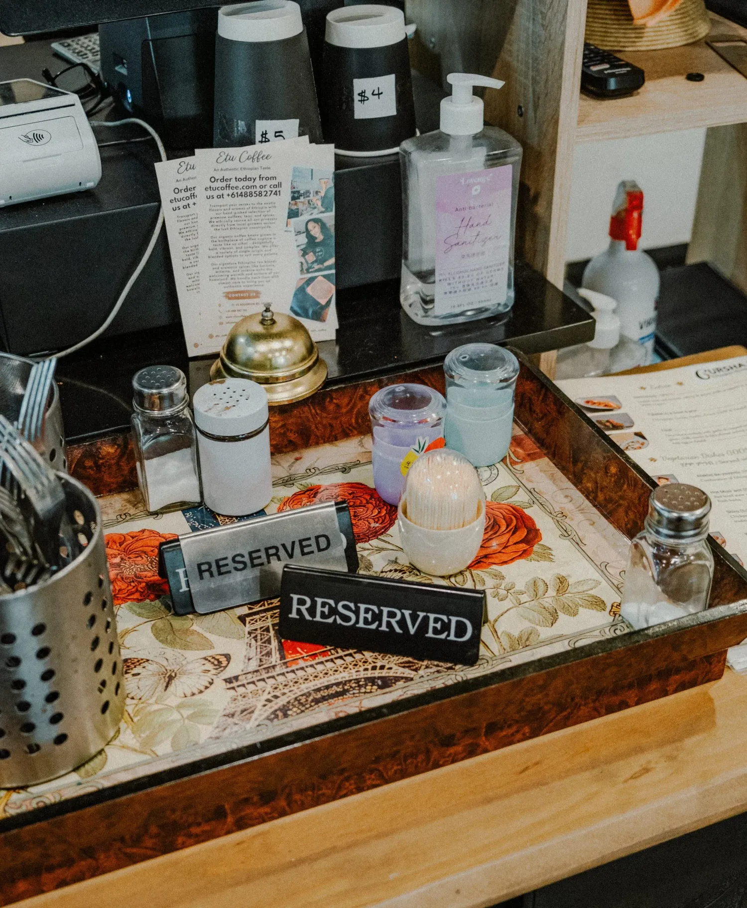 Restaurant host stand with two reserved signs, condiments, and hand sanitizer on a tray.