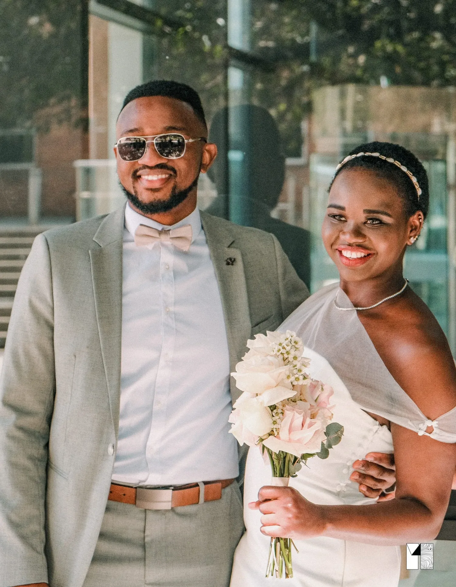 Happy couple on their wedding day, groom in grey suit with bow tie and bride in white dress holding flowers.