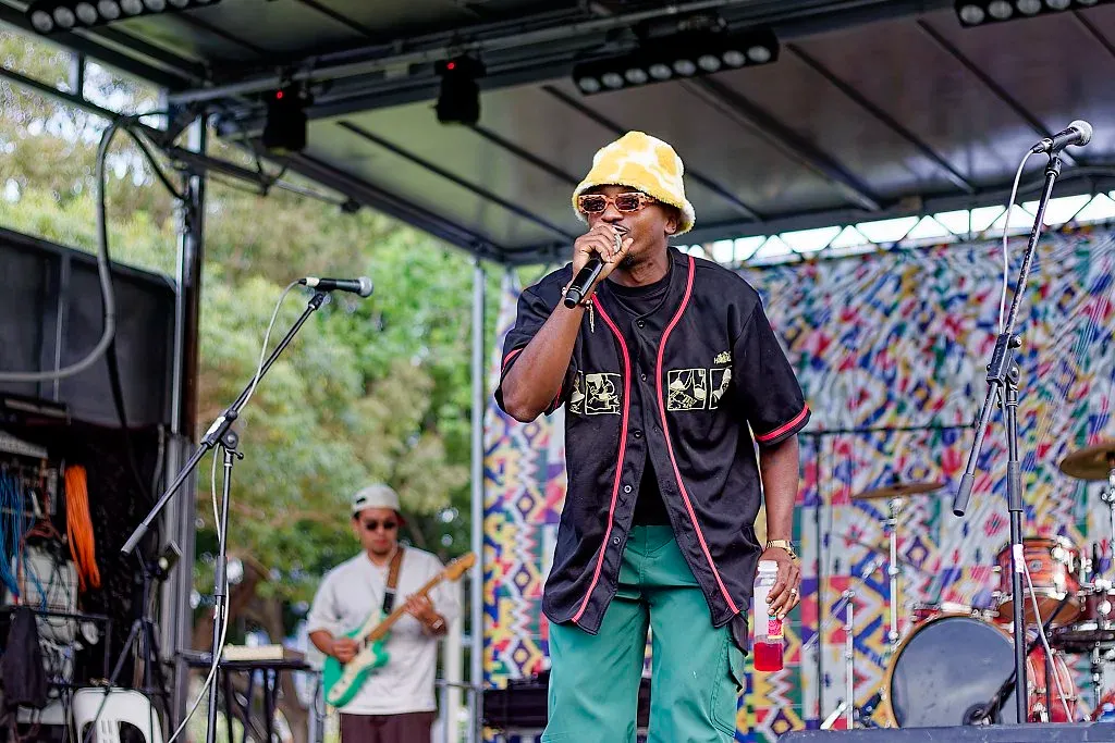Young rapper performing on stage at an outdoor multicultural music festival with colorful backdrop.