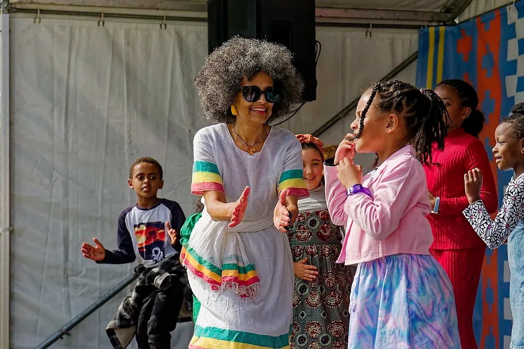 Woman in colorful African dress dancing with children at outdoor multicultural celebration event.
