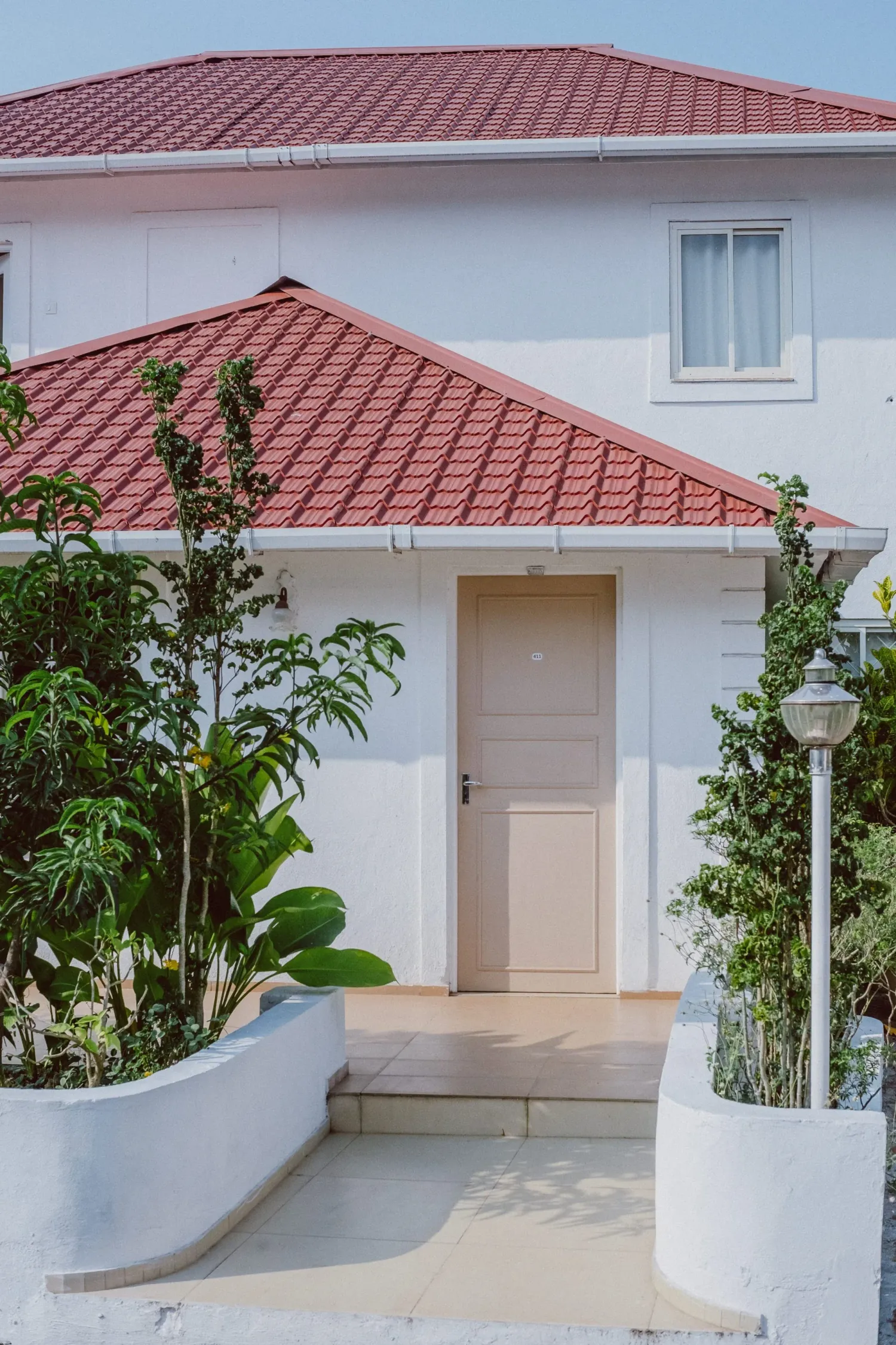 White villa house with red tiled roof surrounded by tropical plants and garden.