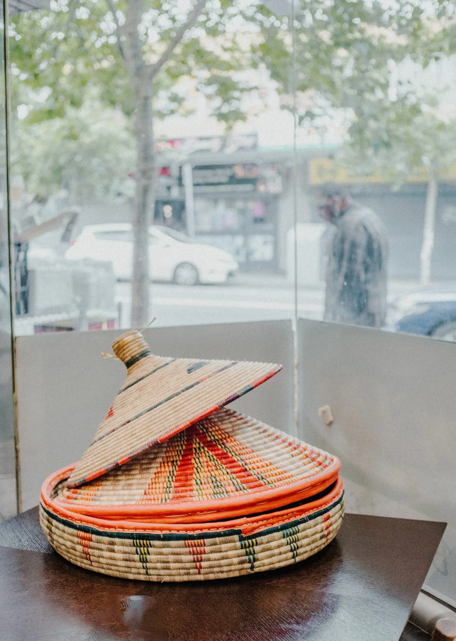 Traditional Ethiopian woven basket with colorful orange and green pattern displayed on a wooden table.