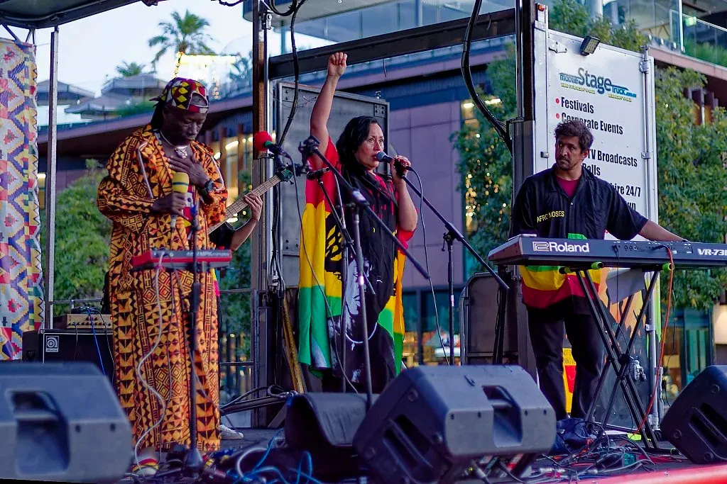 Three musicians performing on stage at a multicultural festival with Roland keyboard and African-inspired outfits.