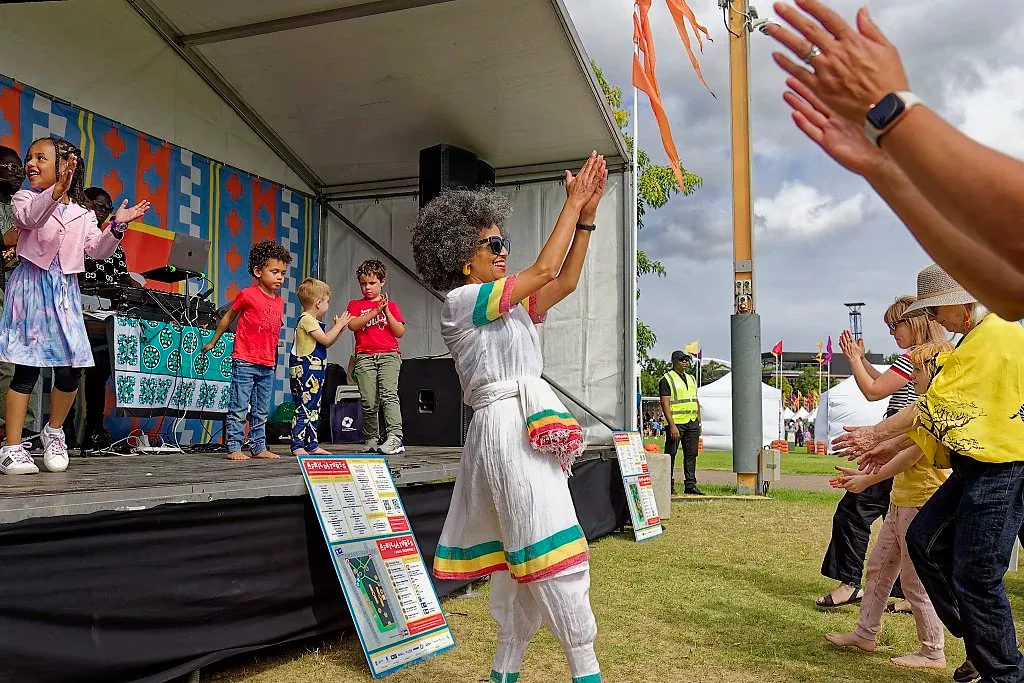 Woman in colorful dress dancing near the stage at an outdoor multicultural festival.