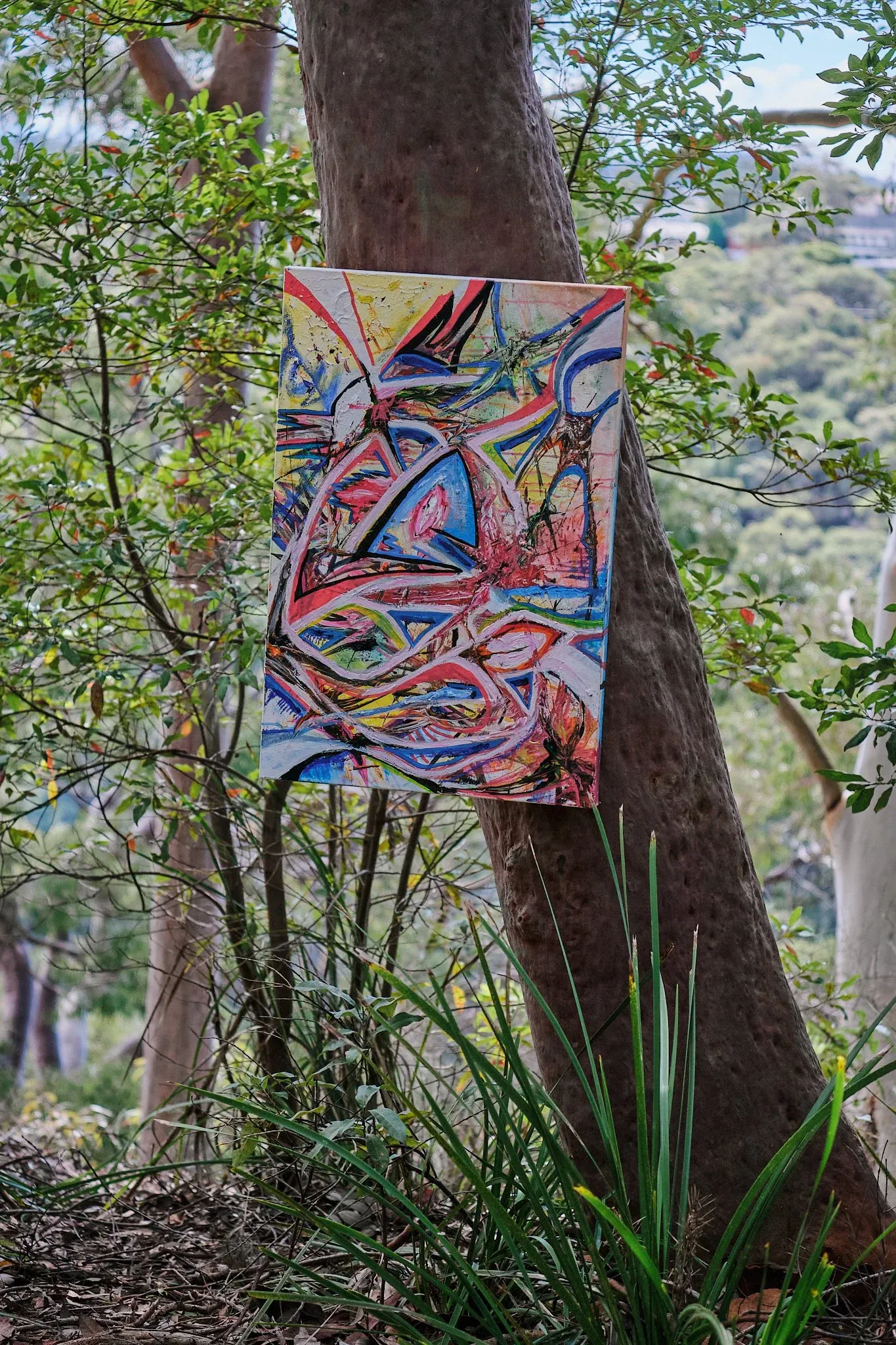 Vibrant abstract painting with swirling colorful lines displayed on outdoor tree trunk.