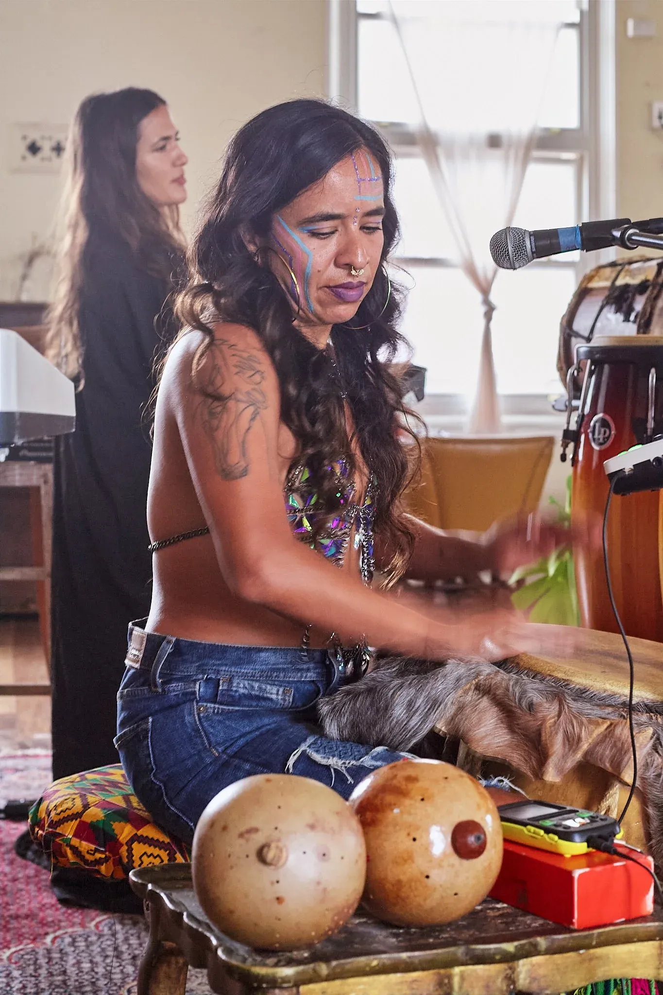 Face-painted woman plays percussion instruments with gourd shakers in a vibrant music session.