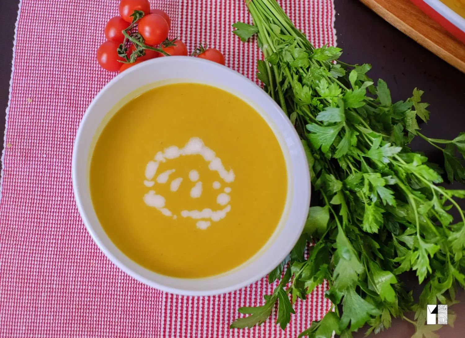 Creamy butternut squash soup garnished with cream swirl, served with fresh parsley and tomatoes.