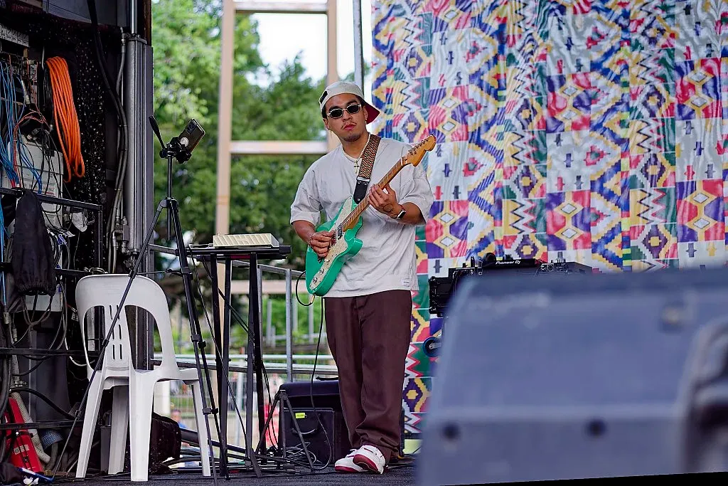 Guitarist playing a green electric guitar on an outdoor festival stage.