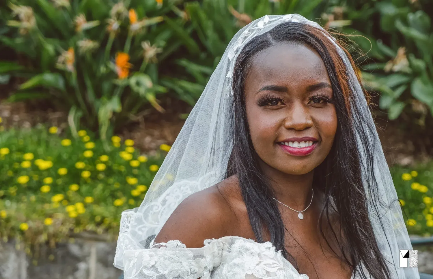 Beautiful bride smiling in a white veil and lace gown with garden flowers in background.