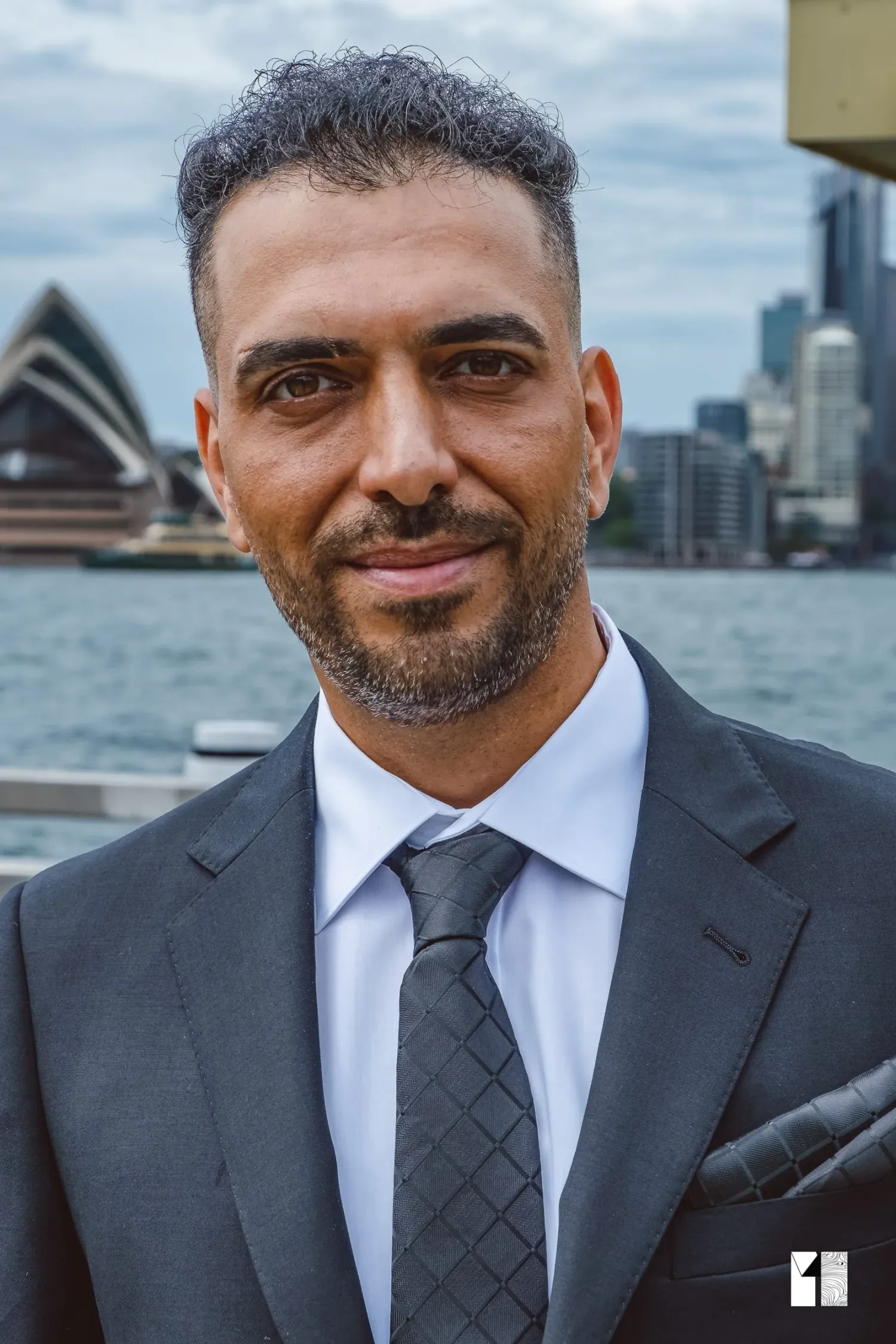 Handsome groom in dark suit poses confidently with Sydney Opera House in background.